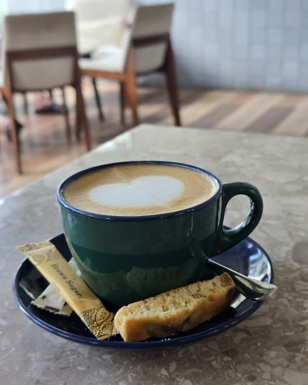 Latte with heart-shaped art in a white cup, served with biscotti on a cafe table